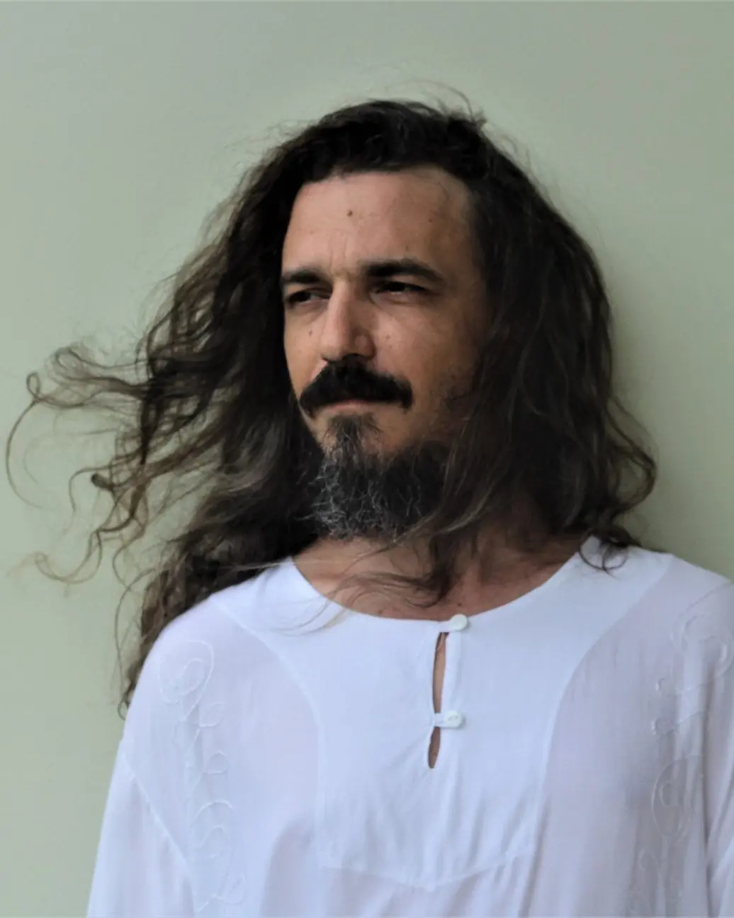 Rodolfo Minari, escritor e professor, de camisa branca e cabelo longo
